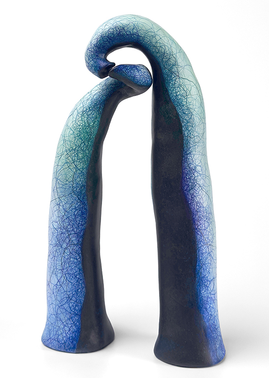 A modern ceramic sculpture featuring two elongated forms that intertwine at the top, with a gradient of blue and teal colors.